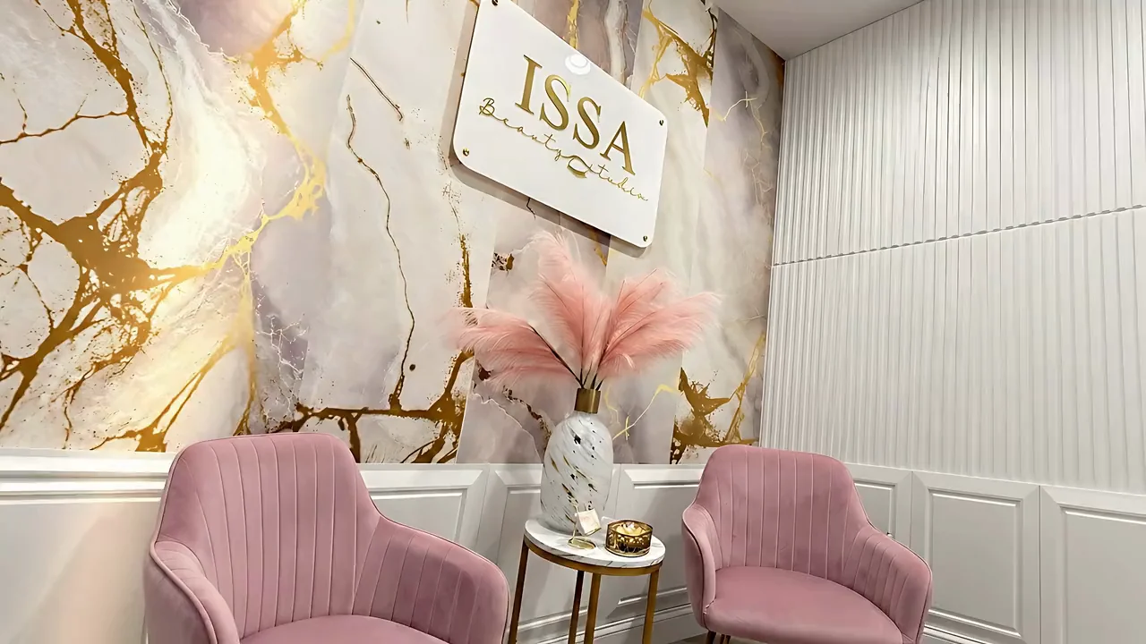The ISSA Beauty Studio gold sign on a white and gold marble wall, with pink pampas and pink velvet chairs
